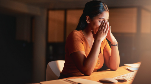 A person sits at their desk with their head in their hands, looking stressed and anxious.