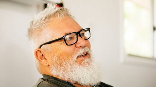 A man wearing black reading glasses smiles at someone off camera