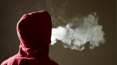 A young person in a red hoody expels a cloud of vape smoke
