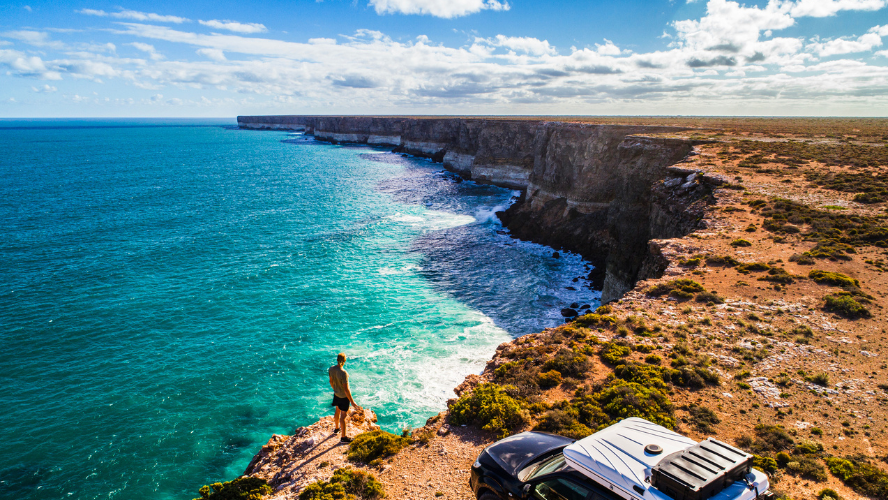 A man stands near the edge of a cliff in front of his 4-wheel drive admiring the Great Australian Bight