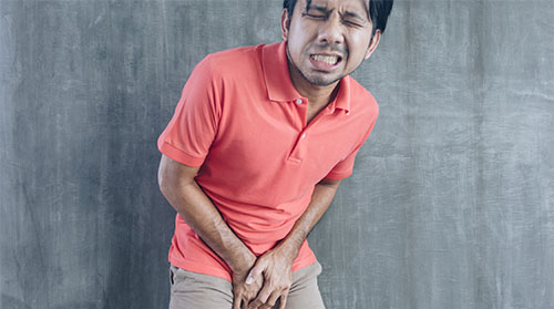 A man with a pained expression holding his testicles with both hands