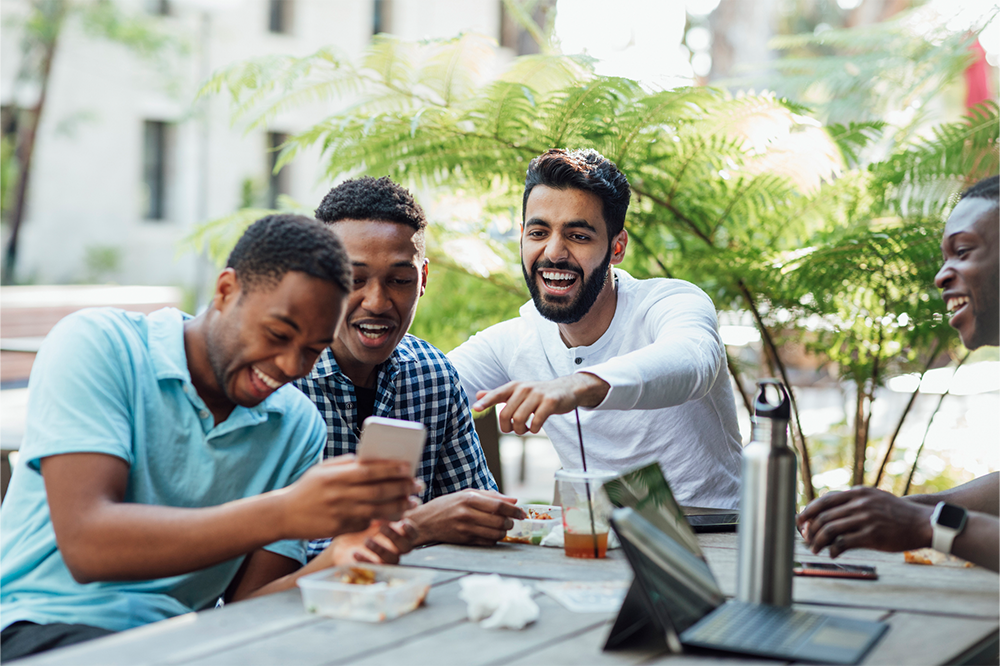 A group of four men laugh at something on a mobile phone