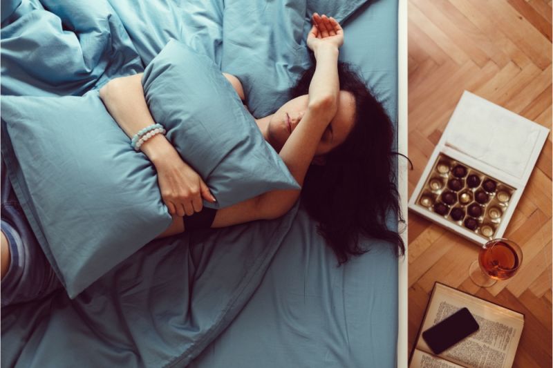 A hungover woman lies in bed with her arm covering her eyes