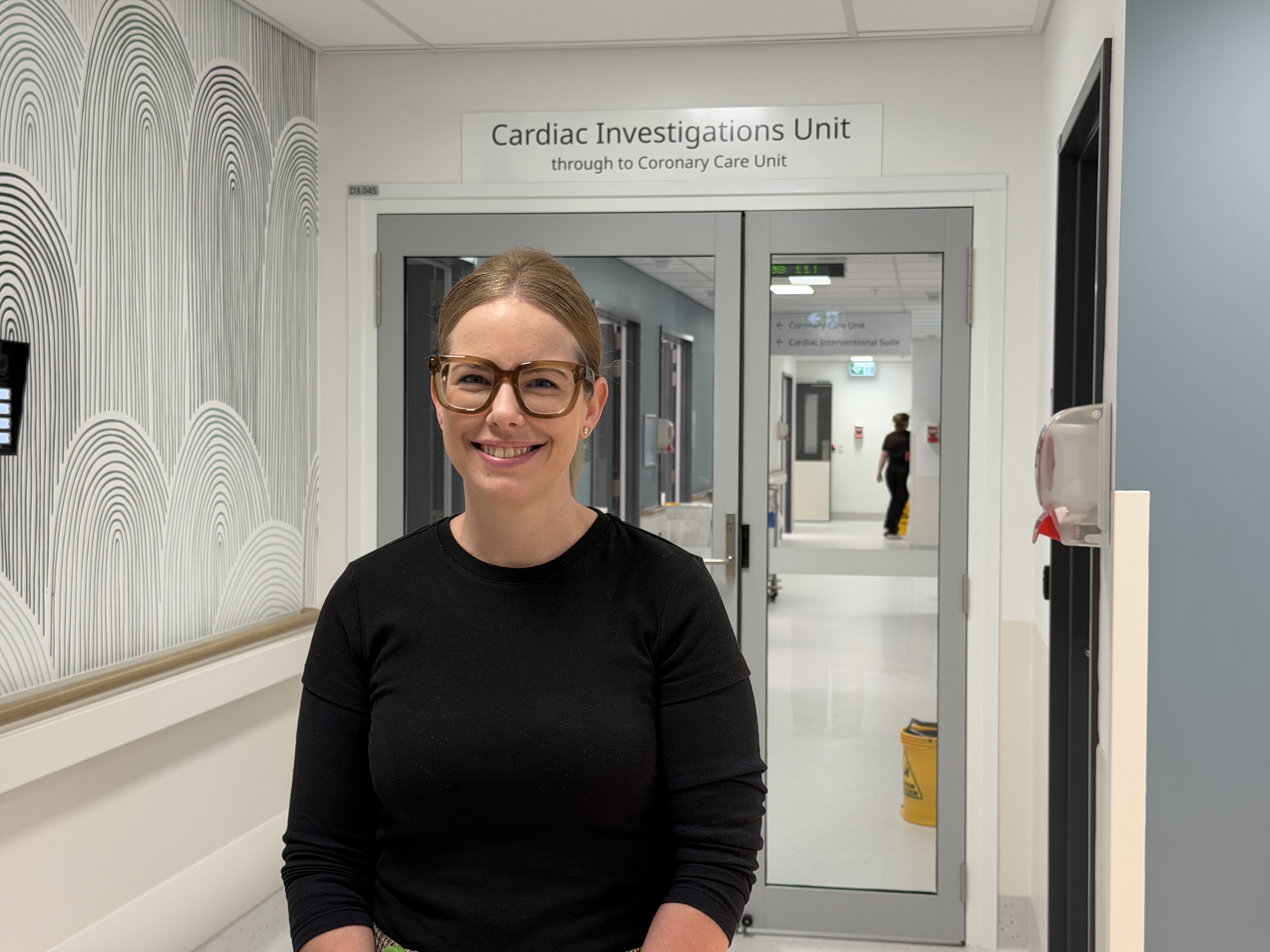 Cardiac Investigations Unit Director Katie Misselbrook smiles at the camera. She stands in front of a sign to the Cardiac Investigations Unit.