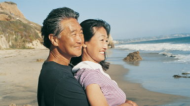 A middle-aged asian couple stares out at the sea from the beach
