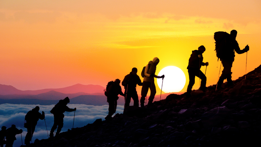 A group of men are climbing up a mountain with the sun behind them.