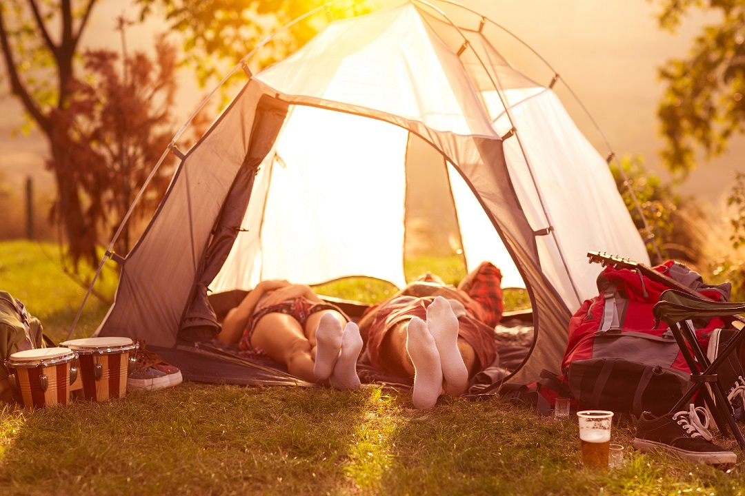 Two people lie in a tent in the afternoon, camping at a music festival.