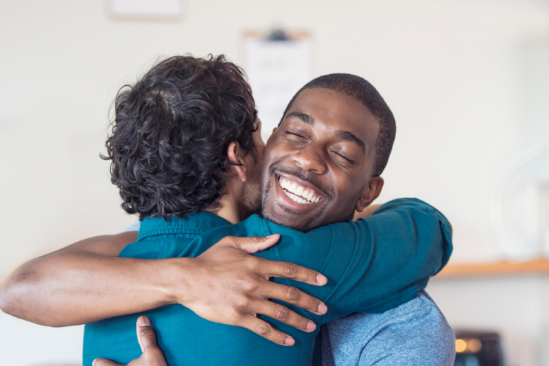 Two smiling men hug lovingly