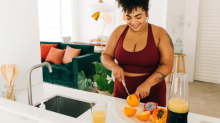 A beautiful woman in maroon sportswear cuts fruit for a juice in her kitchen