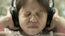 A little girl grimaces at loud noise as she holds headphones over her ears