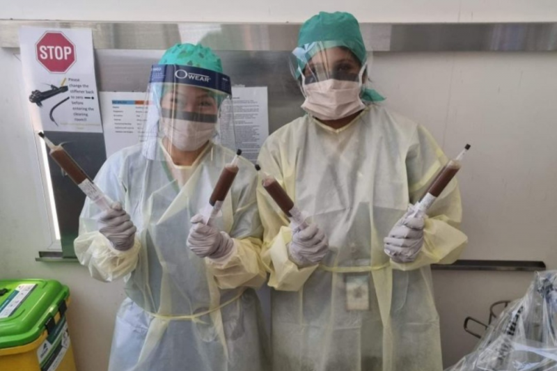 Two nurses from Cairns and Hinterland Hospital and Health Service in PPE holding two large syringes each containing faecal transplant material