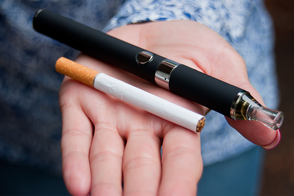 A hand holding a normal cigarette and an e-cigarette next to each other