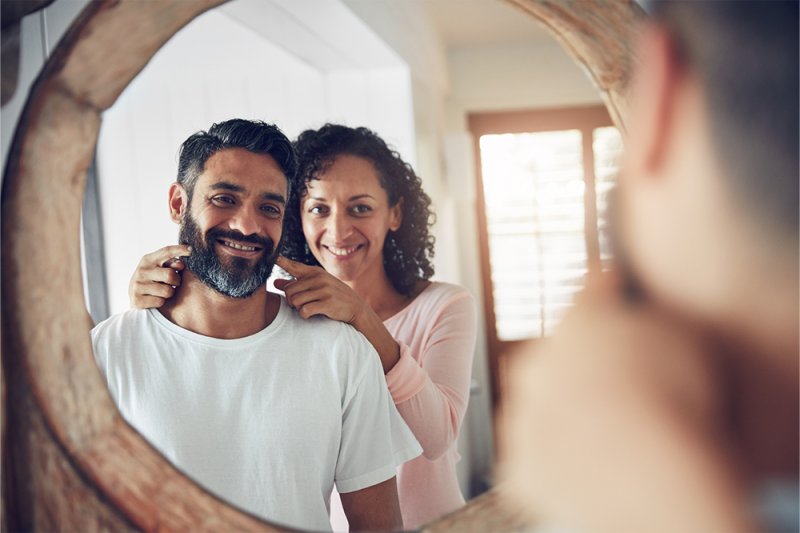 A middle-aged man and woman looking at themselves in a mirror