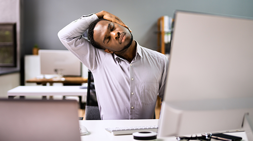 A man sitting behind an office desk and computer screen does yoga neck stretches