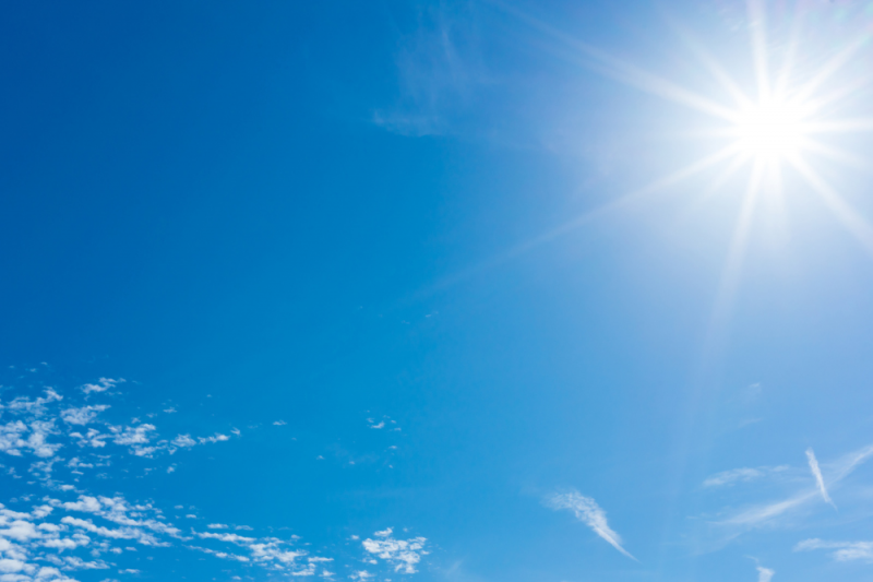 Beautiful blue sky with wispy clouds and a bright sun with white rays