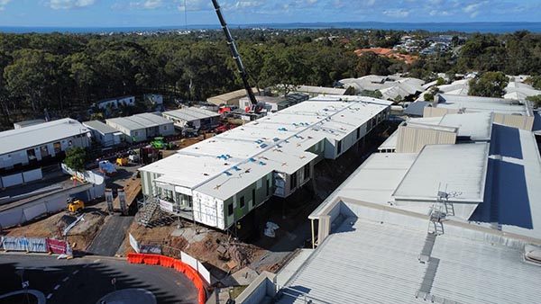 You can see the modular ward in the middle of the image with the main hospital on the right hand side. A crane is in the background, with the site entry and signage in the foreground.