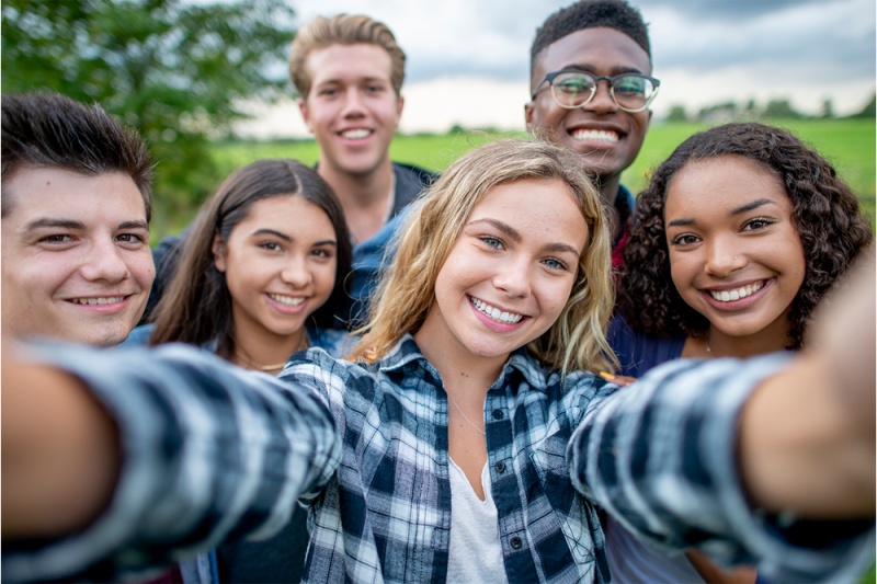 Six young people in a park take a group selfie
