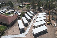 You can see 10 modular staff units in place on-site. There are five on each side and separated by a concrete pathway. The crane used to lower them into place sits to the right of the image. The new modular unit is located beside the old nurses quarters.