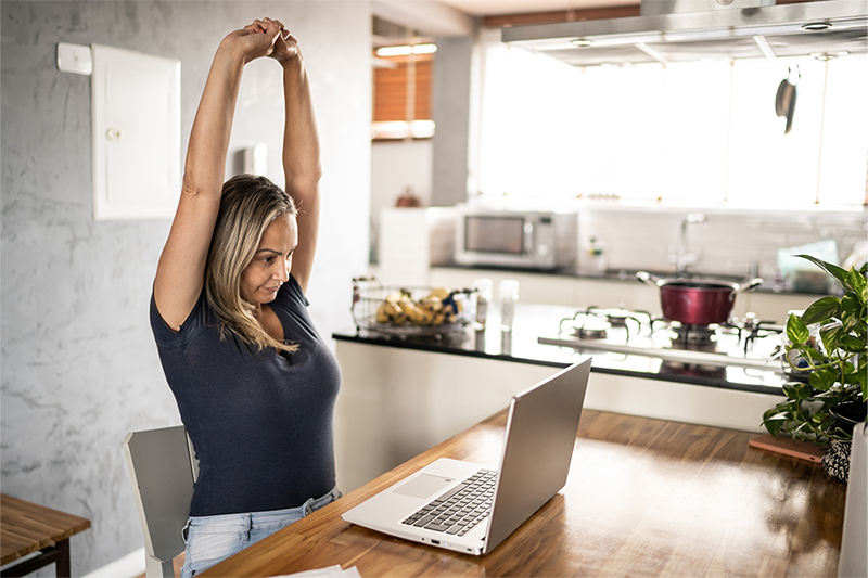 A woman working from home stretches her arms upwards