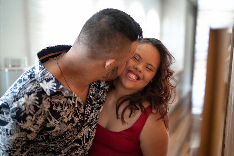 A man kisses his smiling partner on her cheek