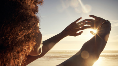 At sunrise a woman on a beach stretches out her clasped hands towards the sun