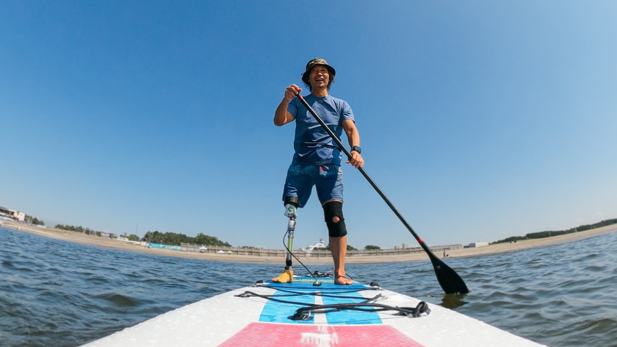 A man with an artificial leg looks happy paddling a standup paddleboard