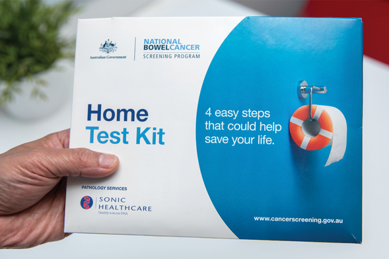 A hand holding a National Bowel Cancer Screening Program test kit box