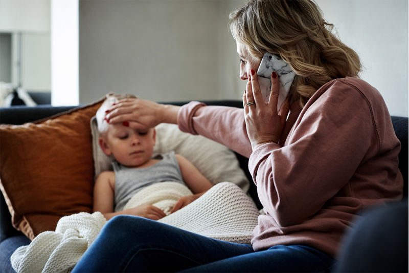 A woman taking care of her little boy who is sick with RSV at home while on the phone to the doctor