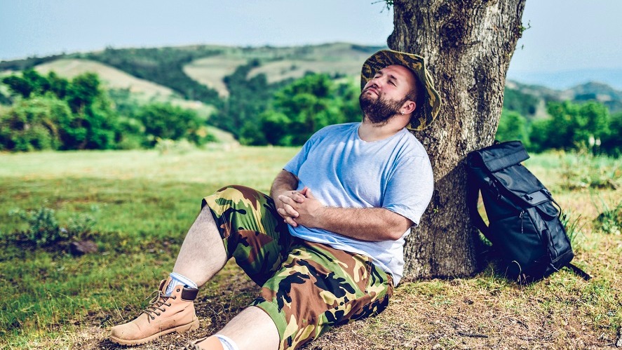 A man lies back against a tree after a hike.