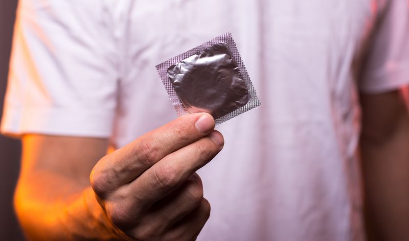 Close up of a man's hand, holding a sealed condom packet