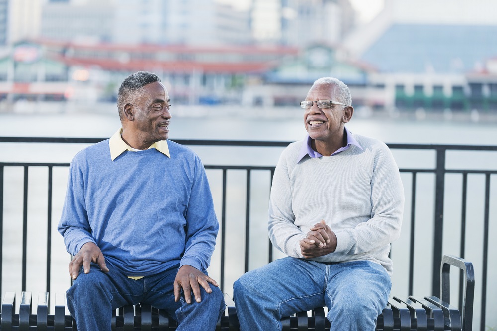 Two friends on a waterside bench talking