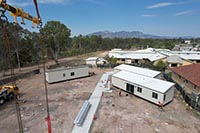 You can see three of the self-contained staff accommodation units in place. There are two on the right hand side and one on the left, separated by a concrete pathway. A crane sits in the foreground and you can see the Biggenden Multipurpose Health Centre in the background white a white roof. The old nurses quarters sits to the side with the terracotta roof.