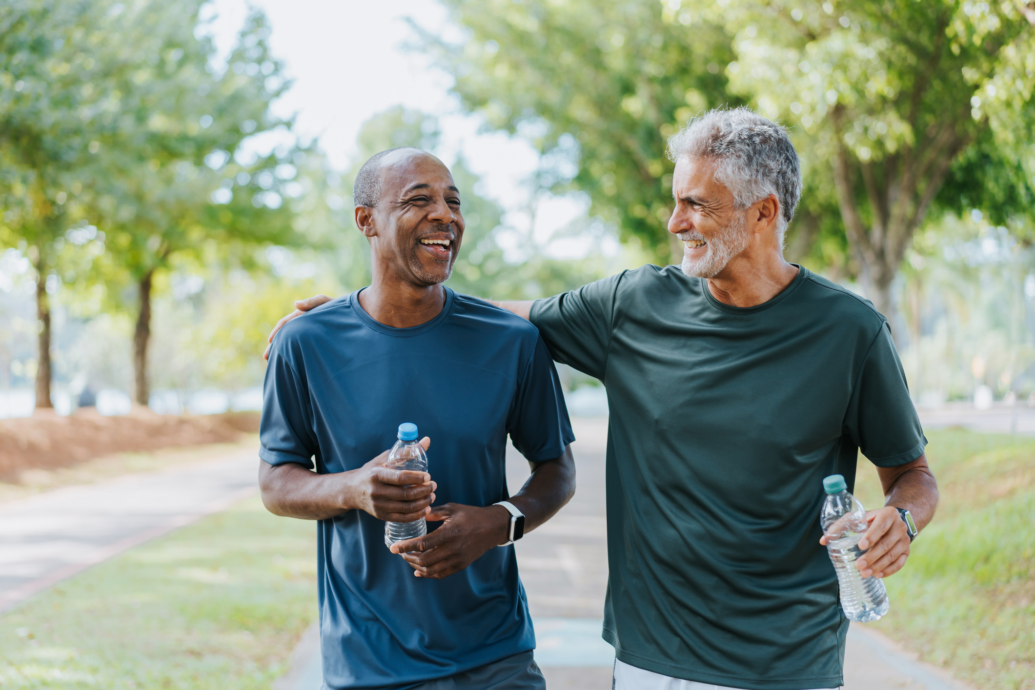 Two men holding water bottles and walking in a park