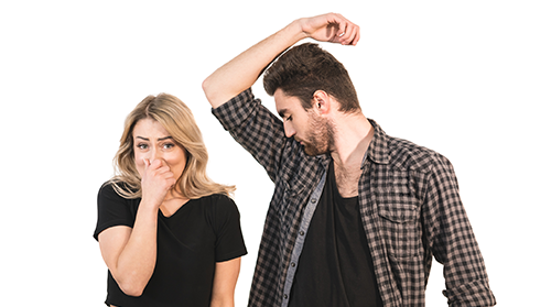 A man sniffs his armpit while a woman pinches her nose with a look of displeasure