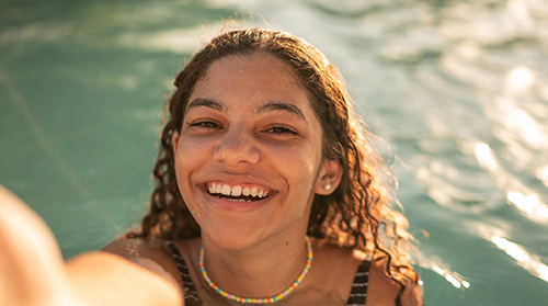 A happy young woman smiles as she takes a selfie in a swimming pool