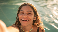 A happy young woman smiles as she takes a selfie in a swimming pool