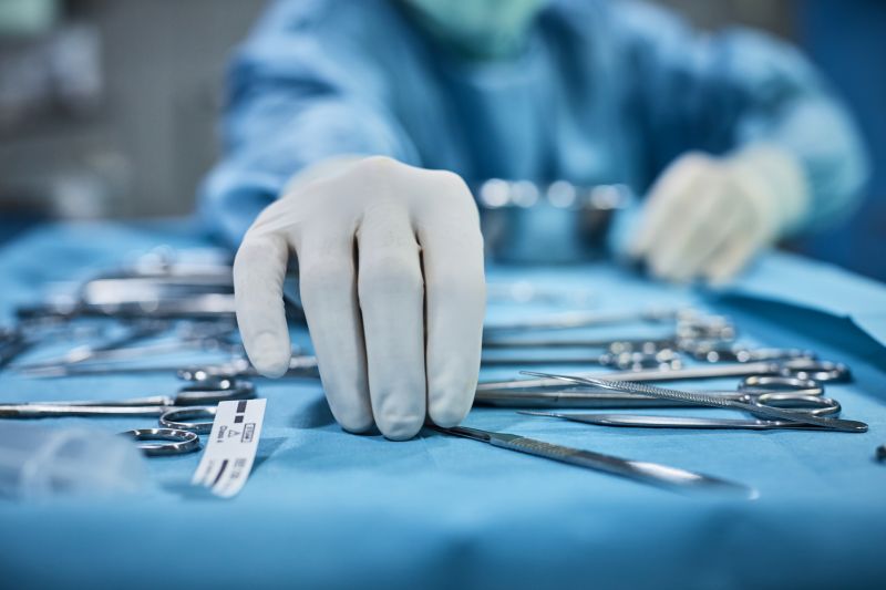 A surgeon's gloved hands picking up surgical instruments. 