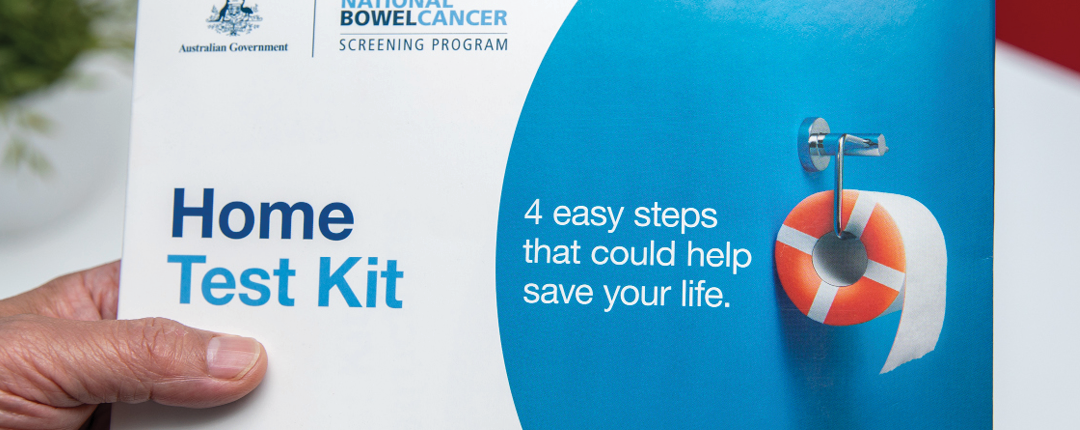 A hand holding a home test kit for the national bowel cancer screening program