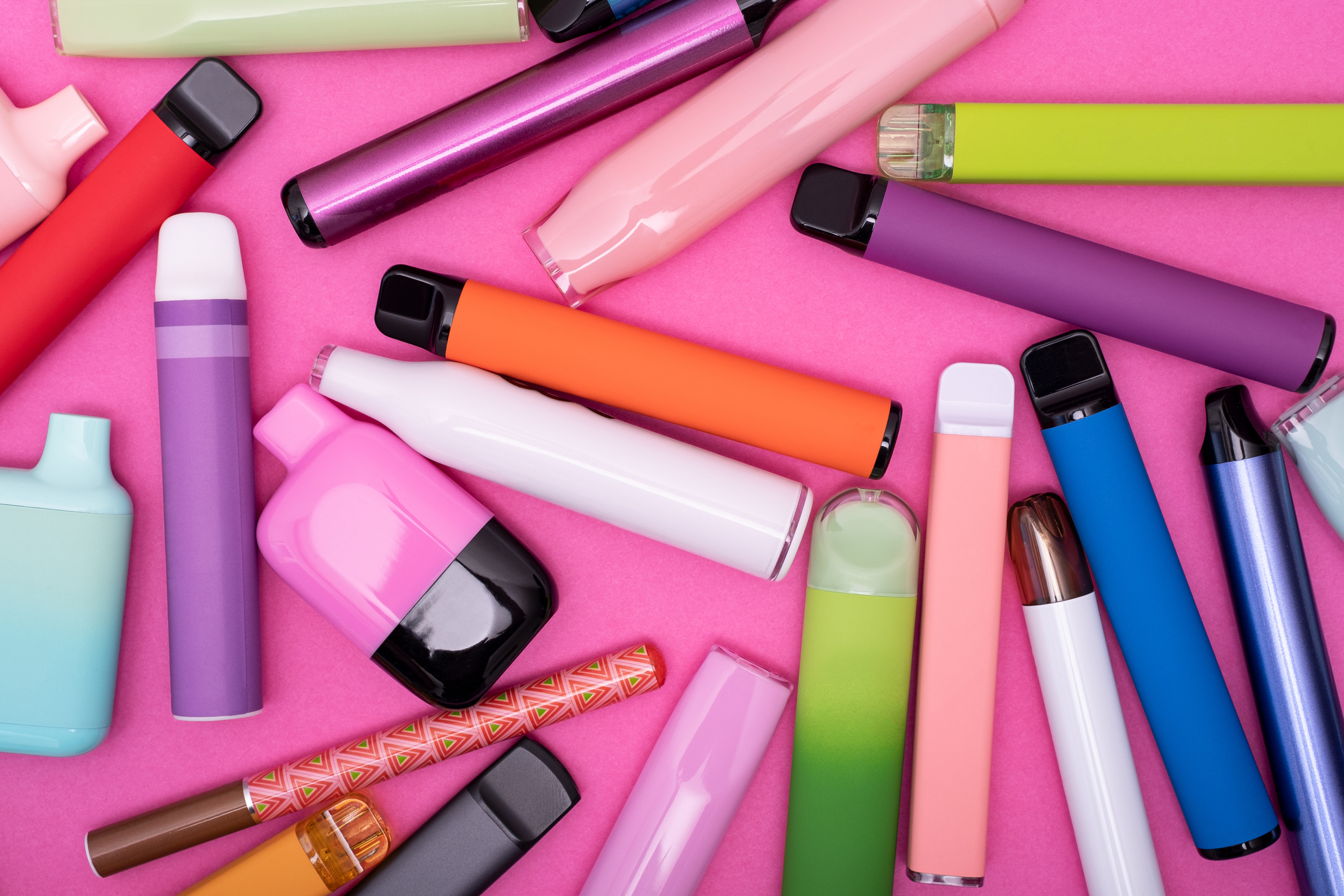 Pink background - multiple different coloured disposable vapes.