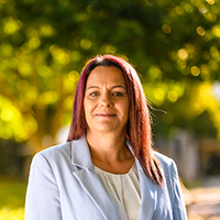 A woman with red hair wearing a blue blazer, smiling confidently at the camera.