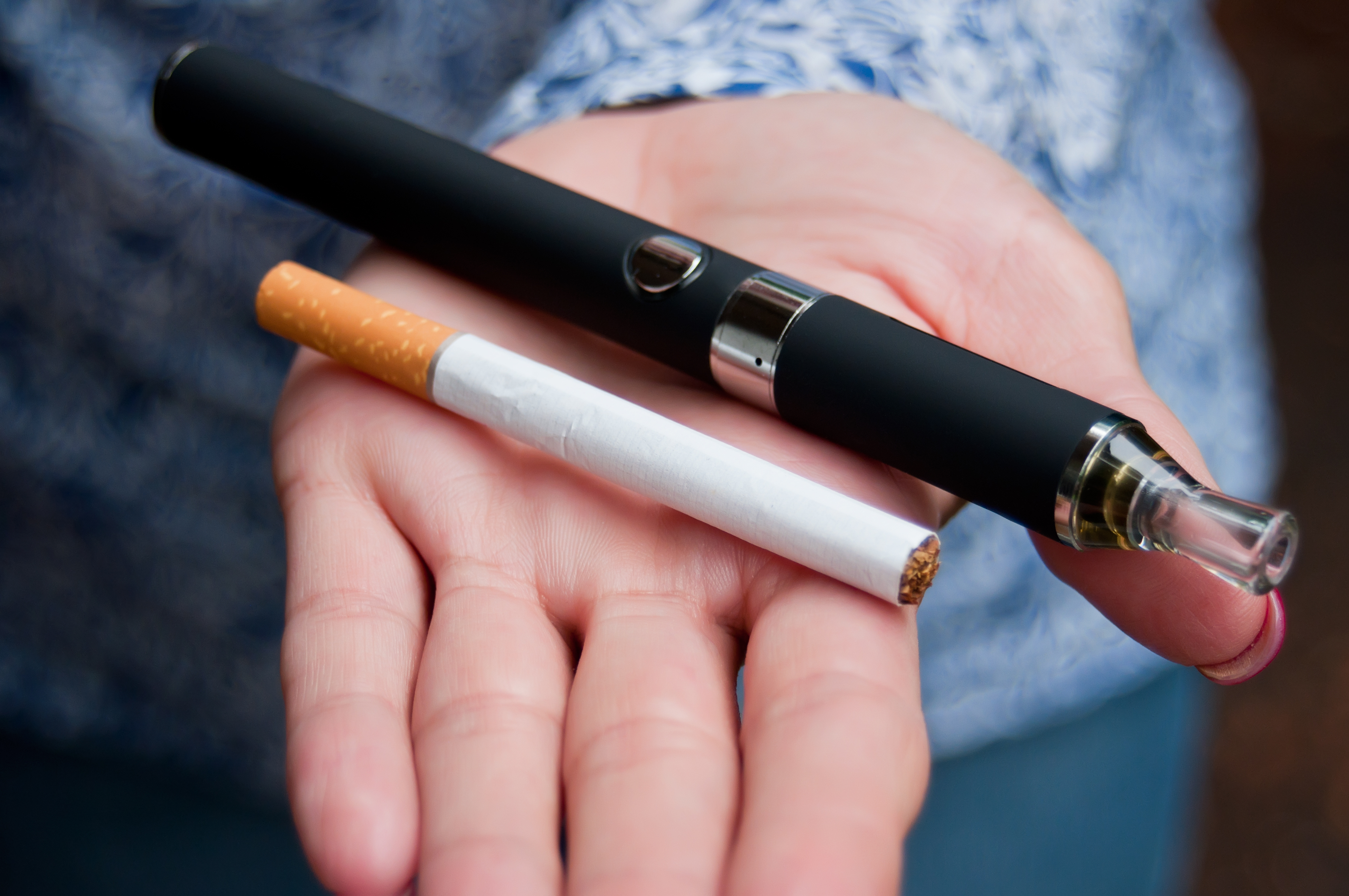 An open hand is holding a black vape and a cigarette 