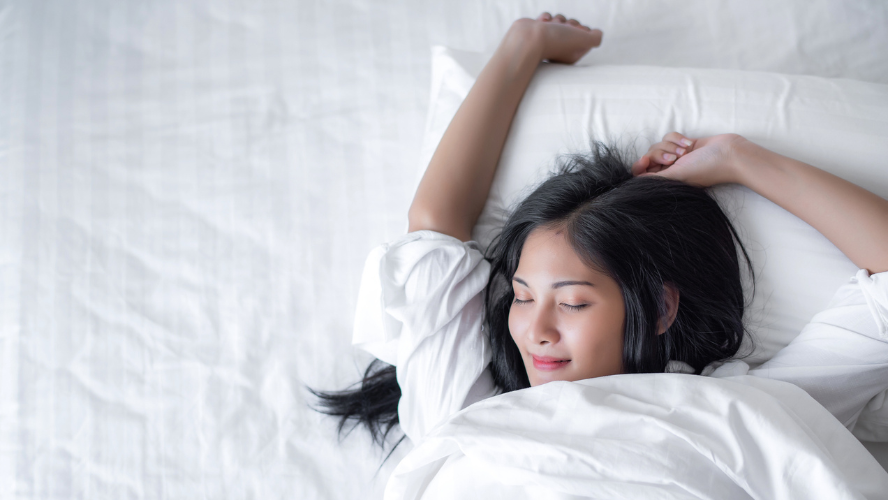 A happy and rested looking woman stretches in bed