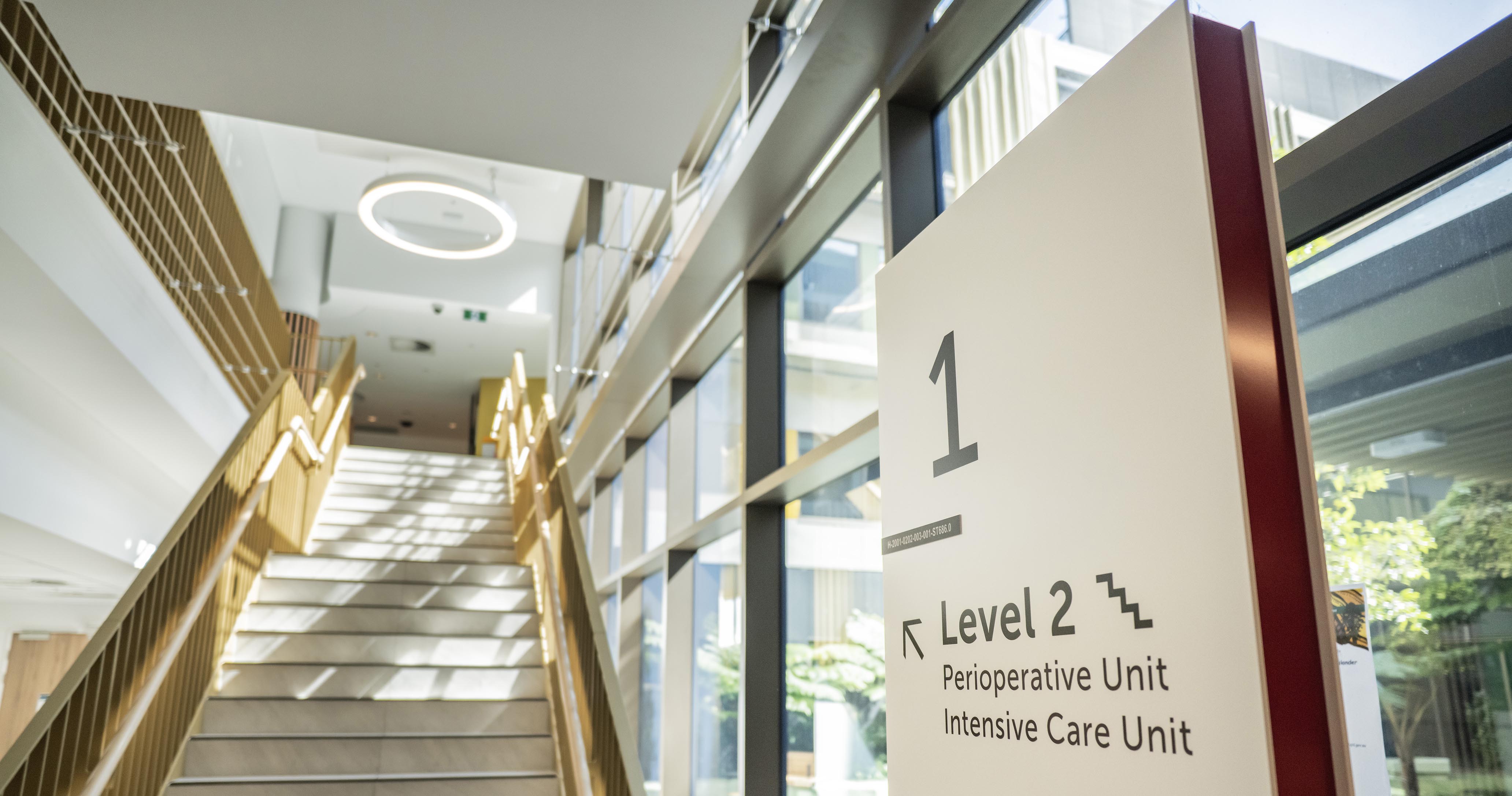 Hospital interior with a staircase and large wayfinding sign indicating Level 2 access to the Perioperative Unit and Intensive Care Unit at Caboolture Hospital.