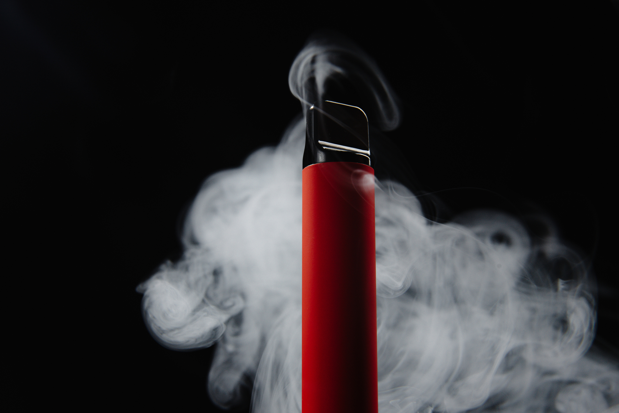 Black background with a red disposable vape with mist coming out of the top.
