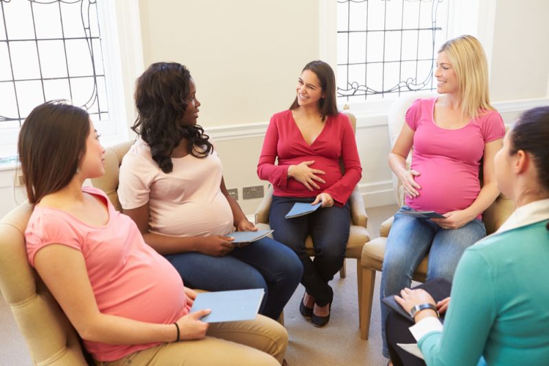 A group of pregnant women sit in an antenatal class, discussing pregnancy with their teacher.