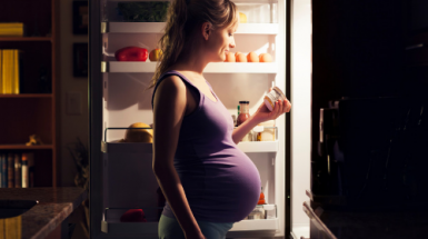 Pregnant woman stands at the fridge and checks a food label