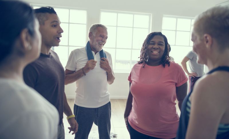 A group of people, young and old, talk after exercising at a gym.