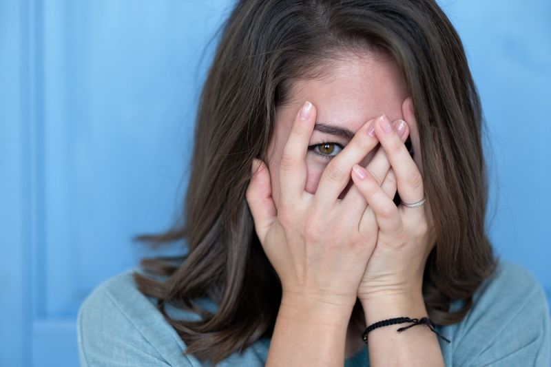 A woman blushing and covering her face with her hands.