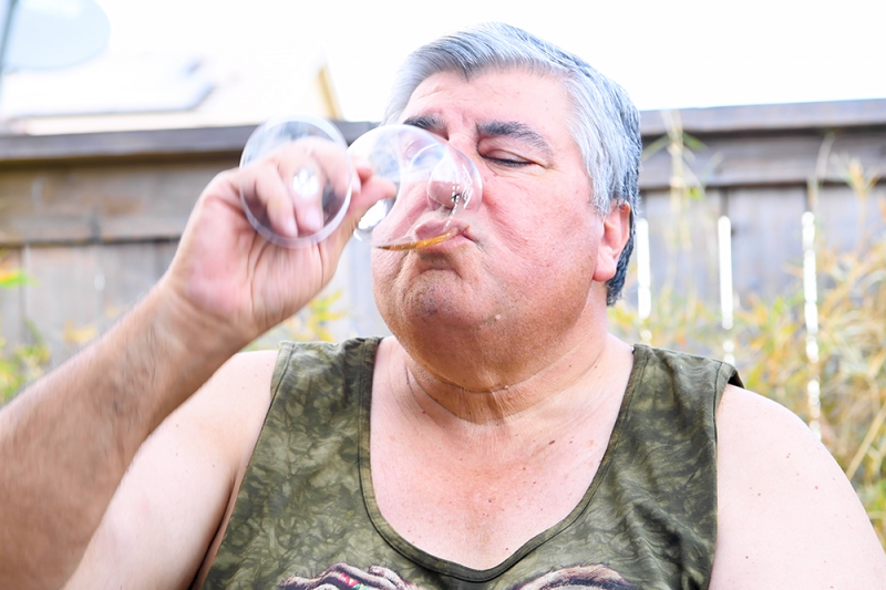 An overweight man finishing a glass of wine