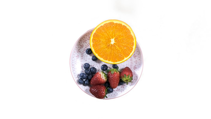 A small white plate of with half an orange and some strawberries and blueberries